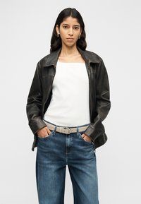 Giacca di pelle nera con collo a risvolto, indossata sopra una maglia bianca con scollo quadrato e jeans a gamba larga azzurri, accentuata da una cintura beige.