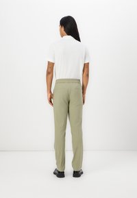 Light olive green pants made of cotton, featuring a relaxed fit, elastic waistband, and two back pockets, worn with a white short-sleeve shirt.