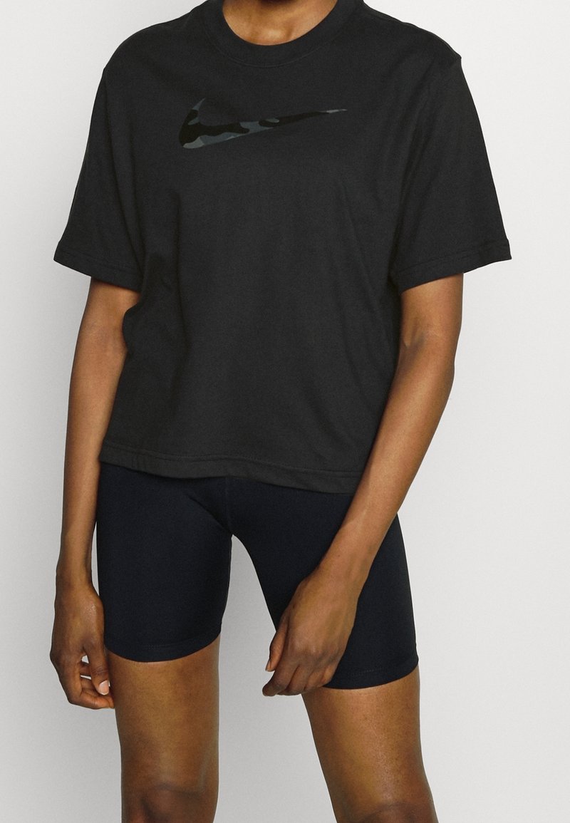 Camiseta de algodón negra con un logo de Nike en camuflaje reflectante en el pecho, combinada con pantalones cortos ajustados negros, enfatizando un look atlético casual.