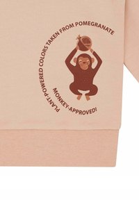 Lichtroze sweatshirt met een bruine aapgrafiek die een granaatappel vasthoudt, omringd door cirkelvormige tekst over plant-geïnspireerde kleuren.