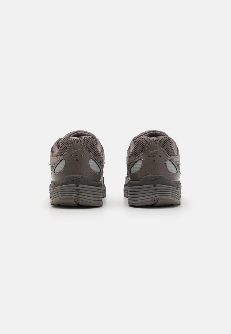 Zapatillas deportivas grises con una parte superior de malla texturizada, suela acolchada y acentos reflectantes en los laterales. La vista trasera muestra un logotipo sutil.