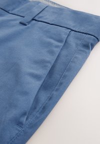 Modre bombažne hlače z gladko teksturo, imajo raven sprednji del, standardno pasnico in lepo zaključene šive.