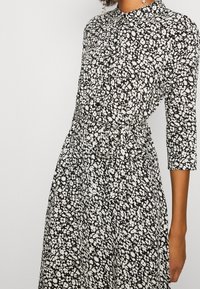 Schwarz-weißer Blumendruckkleid mit einem Kragen, Dreiviertelärmeln und einem taillierten Gürtel für eine definierte Silhouette.