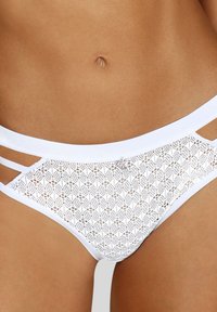 Weiße Spitzenunterwäsche mit floralem Muster, seitlichen Ausschnitten und einem glatten Bund für ein zartes und strukturiertes Design.