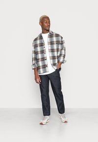 Camisa de flanela xadrez em tons de azul e branco, calças de denim cinza, T-shirt branca por baixo e ténis cinzentos com detalhes.