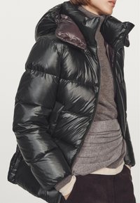 Black puffer jacket with a shiny finish, hood, and zip closure. Features quilted sections, ribbed cuffs, and a purple lining.