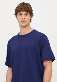 Tamsiai mėlynas medvilninis marškinėliai su trumpomis rankovėmis ir apvaliu iškirpimu, pasižymintys lygiu paviršiumi ir standartiniu pritaikymu.