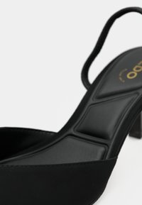 Fekete, magas sarkú szandál elegáns kialakítással, texturált talppal, vékony boka pánttal és alacsony blokksarokkal.