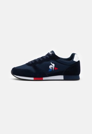 Baskets bleu marine avec des accents blancs, rouges et bleus sur la semelle, un patch blanc au talon et un logo coq blanc sur le panneau latéral.