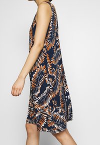 Robe sans manches florale en marine, avec des motifs de feuilles orange et blancs, coupe ample, tissu doux et design mi-long.
