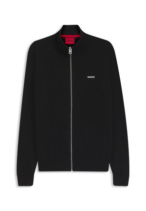 Črni pulover z zadrgo, rebrastim ovratnikom in manšetami, majhen bel napis "HUGO" na levem prsnem delu ter rdeča etiketa na ovratniku.
