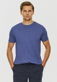 Niebieska bawełniana koszulka z okrągłym dekoltem i kr�ótkimi rękawami, o gładkiej fakturze i luźnym kroju. Noszona z ciemnymi spodniami.