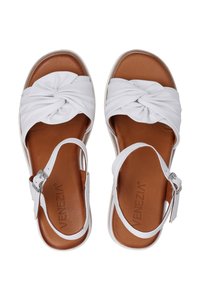 Witte sandalen met geknoopte leren bandjes en een bruine binnenzool. Verstelbare enkelband met een zilveren gesp. Platte zool met een lichte textuur.