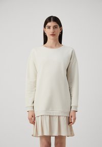 Felpa color crema con scollo rotondo e spalle cadenti, abbinata a una gonna a pieghe leggera, caratterizzata da un tessuto morbido e una vestibilità rilassata.