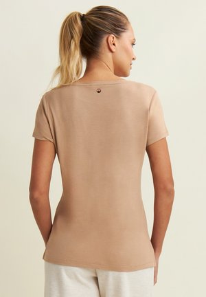 T-shirt corta beige con texture liscia, scollo rotondo e un piccolo logo sul retro. Silhouette aderente, design minimalista.