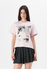 Rosa bomulls t-skjorte med et svart-hvitt grafikk av en kvinnelig figur som spiller gitar, med en sommerfugl og navnet "Dolly" trykt over.