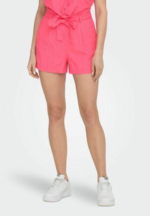 Shorts en lin roses avec une taille ceinturée, présentant une coupe décontractée et des poches latérales. Portés avec des baskets blanches pour le contraste.