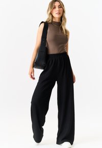Brown sleeveless top with a high neck, textured black wide-leg pants, and a black shoulder bag. White sneakers complete the outfit.