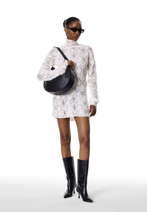 White lace dress with long sleeves, black structured handbag, and black knee-high pointed boots. Accessories include dark sunglasses and earrings.