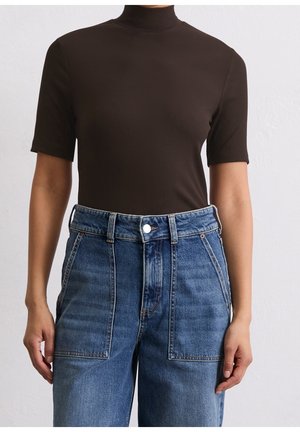 Persoon draagt een nauwsluitende zwarte korte mouw coltrui, ingestopt in een high-waist blauwe spijkerbroek met grote voorzakken.