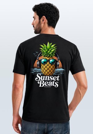 Mann trägt schwarzes T-Shirt mit bunter Grafik einer Ananas mit Sonnenbrille und Kopfhörern über dem Text "Sunset Beats."