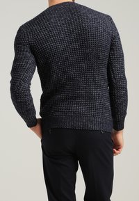 Granatowy sweter dzianinowy o fakturowanym wzorze, z prążkowanymi mankietami i dołem oraz klasycznym okrągłym dekoltem, w połączeniu z ciemnymi spodniami.