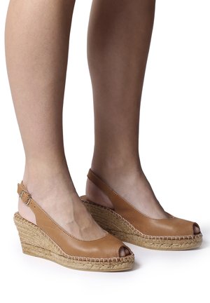 Fødder iført beige læder sandaler med kilehæl, peep-toe, flettede jute-såler og stropper bagpå med spænder.