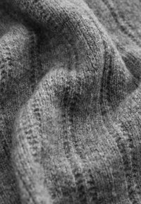 Grau gestrickter Stoff mit einer weichen Textur, der wellenförmige Linien und unterschiedliche Stichmuster aufweist und ein reichhaltiges, schichtartiges Erscheinungsbild erzeugt.