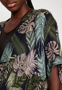 Kimono floral con fondo azul marino, con grandes patrones de hojas verdes y beige, tejido ligero y diseño de corte holgado.