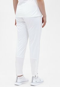 Weiße Sporthose mit schlankem Schnitt, mit einer glatten Textur, seitlichen Reißverschlüssen an den Knöcheln und kombiniert mit weißen Sneakers.