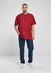 Rød oversized t-skjorte med rund hals og slitte kanter, kombinert med blå denimjeans og hvite joggesko.