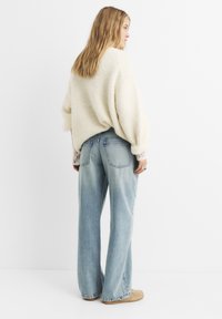 Maglione crema peloso, jeans a vita alta blu chiaro a gamba larga, tasche posteriori visibili, vestibilità rilassata, con scarpe casual di colore neutro.