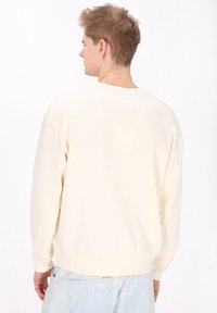Lichte crèmekleurige katoenen sweatshirt met een ronde halslijn, verlaagde schouders en ribgebreide boorden. De achterkant is glad met minimale ontwerpelementen.
