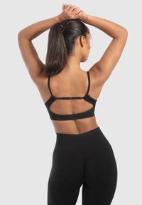 Zwarte sportbeha met dunne bandjes, verstelbare sluiting aan de achterkant en een subtiele geribbelde textuur. Gecombineerd met hoge zwarte leggings.