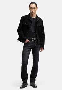 Czarna zamszowa kurtka z kołnierzem, przednimi kieszeniami i zapięciami na guziki, zestawiona z czarnym t-shirtem i ciemnymi dżinsami. Czarne skórzane buty.