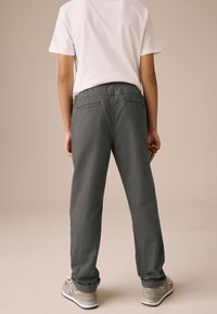 Pantalon gris à coupe décontractée, avec poches arrière et taille élastique, associé à des baskets gris clair et un t-shirt blanc.
