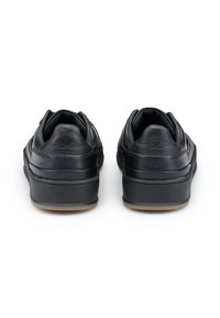 Un paio di sneakers nere in pelle viste da dietro, caratterizzate da colli imbottiti e dettagli testurizzati sul tallone, su sfondo bianco.