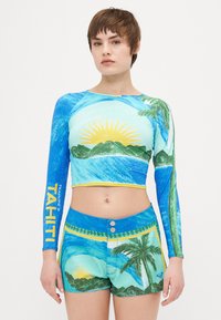Långärmad croppad rash guard och shorts-set med livfulla blå och gröna tropiska grafiska mönster, med gula accenter och detaljer.