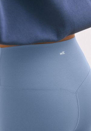 Close-up of light blue high-waisted leggings with white "self." logo and a cropped dark blue top.