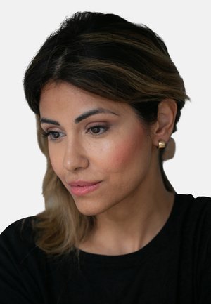 Nahaufnahme einer Person mit langen, hellbraunen Haaren, die goldene Creolen und ein schwarzes Shirt trägt. Sie hat eine glatte Hautstruktur und dezentes Make-up.