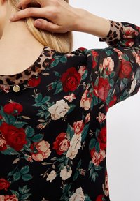 Blusa nera a fiori con rose rosse e crema, foglie verdi, colletto a stampa leopardata e dettaglio di bottone dorato sul retro del collo.