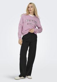 Lichtroze sweatshirt met de tekst "HARVEST MAKER", geribbelde manchetten, relaxte pasvorm, gecombineerd met zwarte wijde broek en witte sneakers.