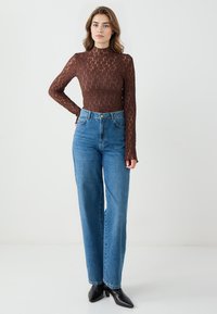 Kastanjebruine lange mouwen top met een textuurpatroon, gecombineerd met hoge taille blauwe rechte jeans en zwarte puntige hakken.