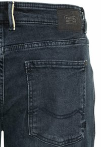 Granatowe dżinsy mają gładką fakturę, standardowe tylne kieszenie oraz czarną skórzaną naszywkę z logo na pasku.