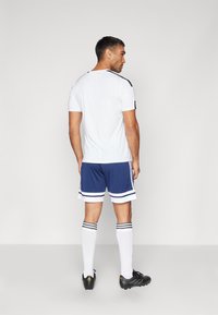 Vit träningströja med svarta detaljer, blå shorts med vita ränder, knähöga vita strumpor med svarta ränder, och svarta fotbollsskor.