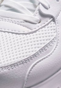 Witte sneaker met gestructureerd leer en meshpanelen, platte veters en verhoogde stiksels aan de zijkant voor extra detail.