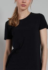 Black t-shirt made of soft fabric, featuring short sleeves and a round neckline. The fit is relaxed with a smooth texture and minimal detailing.