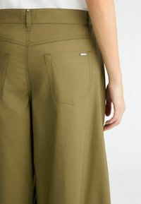 Pantalons amples vert olive en tissu léger, dotés de deux poches arrière et de détails de couture subtils.