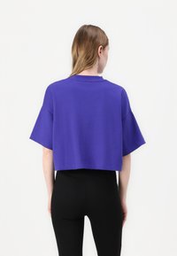 Top corto a manica corta in cotone viola solido. Presenta un collo a giro e una vestibilità rilassata, abbinato a leggings neri aderenti.