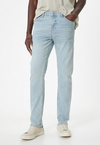 Jeans de mezclilla azul claro con diseño de pierna recta, cuatro bolsillos y una textura sutilmente desgastada. Llevados con zapatillas beige.